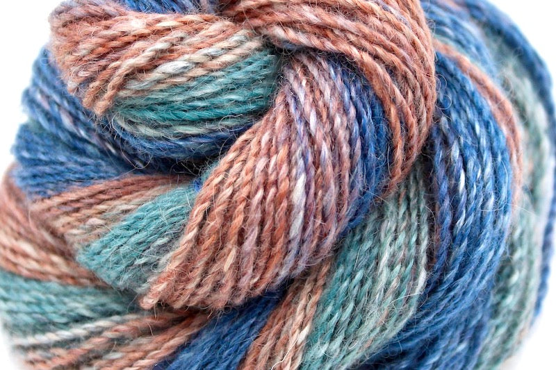 A close up view of a one of a kind, gradient skein of multicolored Royal Blue, Mauve, Reddish Orange, Light Teal and Dark Teal self-striping wool Yarn. 