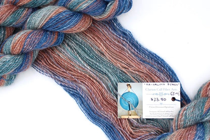 A one of a kind, hand dyed gradient skein of multicolored Royal Blue, Mauve, Reddish Orange, Light Teal and Dark Teal self-striping wool Yarn draped diagonally across the frame, so you can really see the color play. 