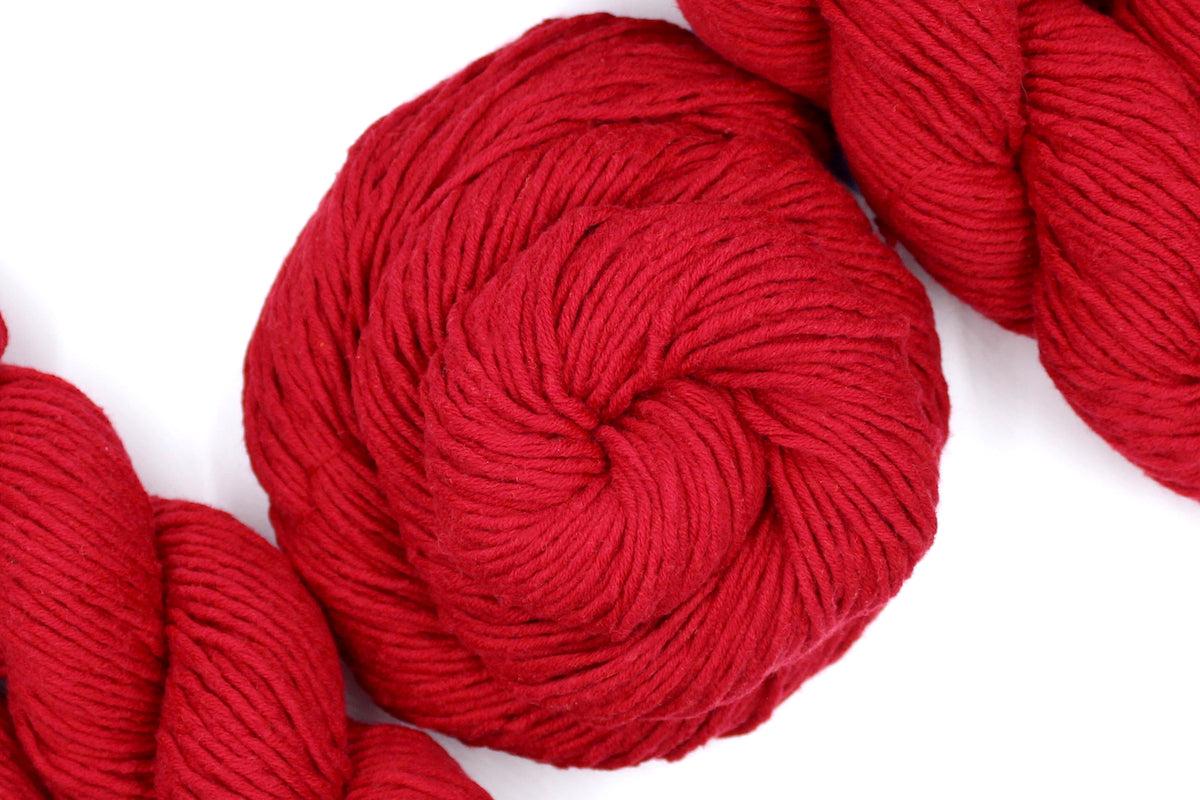 A skein of Vegan, Red, 100% Cotton, Worsted Weight Yarn recycled by hand from unwanted sweaters swirled attractively in the center of the frame. 