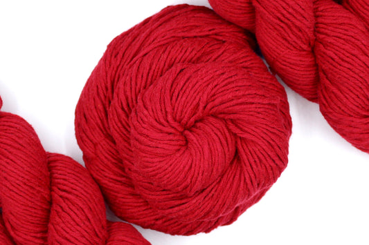 A skein of Vegan, Red, 100% Cotton, Worsted Weight Yarn recycled by hand from unwanted sweaters swirled attractively in the center of the frame. 