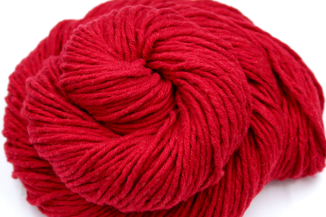 A close up shot of a skein of Vegan, Red, 100% Cotton, Worsted Weight Yarn recycled by hand from unwanted sweaters beautifully coiled in the center of the frame. 