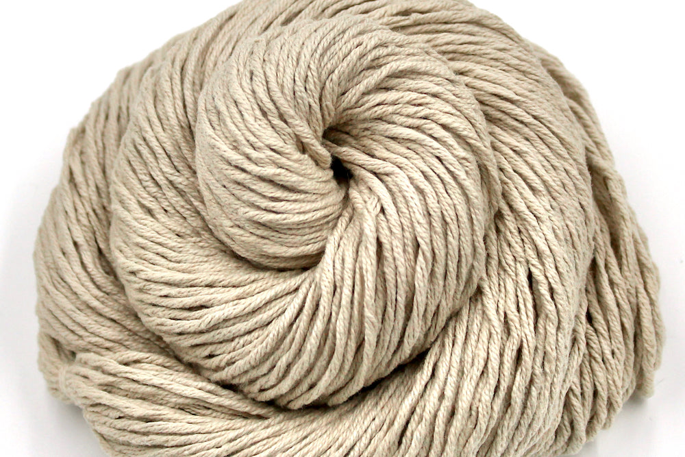 A close up shot of a skein of Vegan, light beige, 100% Cotton, Worsted Weight Yarn recycled by hand from unwanted sweaters beautifully coiled in the center of the frame. 
