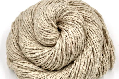 A close up shot of a skein of Vegan, light beige, 100% Cotton, Worsted Weight Yarn recycled by hand from unwanted sweaters beautifully coiled in the center of the frame. 