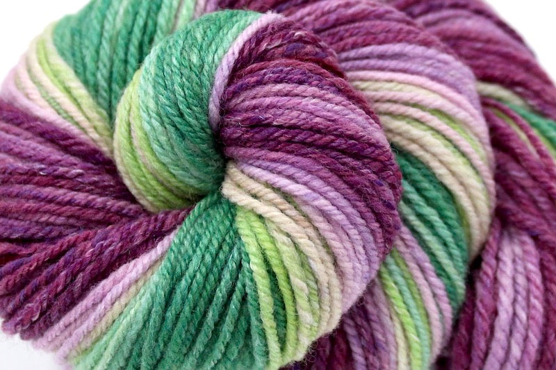 A close up view of a one of a kind, gradient skein of multicolored Magenta, Orchid Pink, Light Pink, Light Green, Lime Green, and Kelly Green self-striping wool Yarn. 