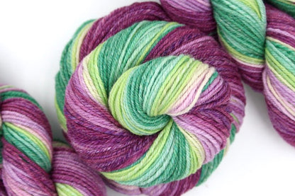 A one of a kind, hand dyed gradient skein of multicolored Magenta, Orchid Pink, Light Pink, Light Green, Lime Green, and Kelly Green self-striping wool Yarn coiled attractively in the center of the frame. 