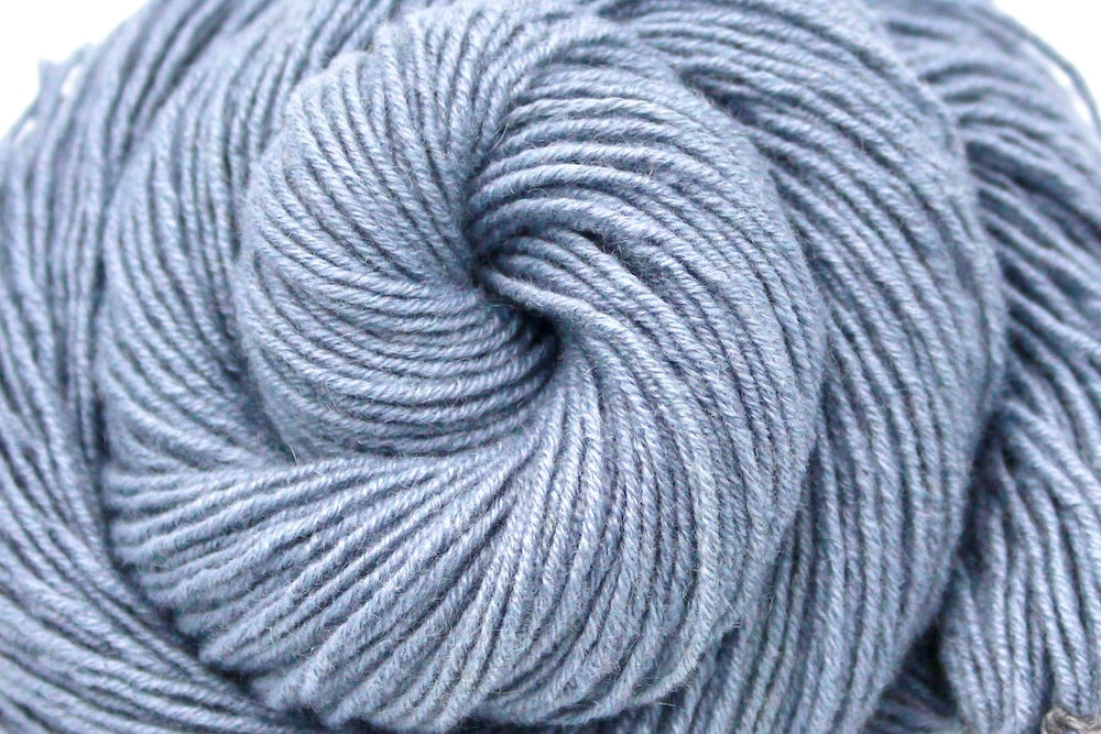 A close up shot of a skein of Light Silver Grey, 100% Cashmere wool, Sport weight Yarn recycled by hand from unwanted sweaters beautifully coiled in the center of the frame. 