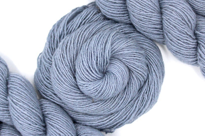 A skein of Light Silver Grey, 100% Cashmere wool, Sport weight Yarn recycled by hand from unwanted sweaters swirled attractively in the center of the frame. 