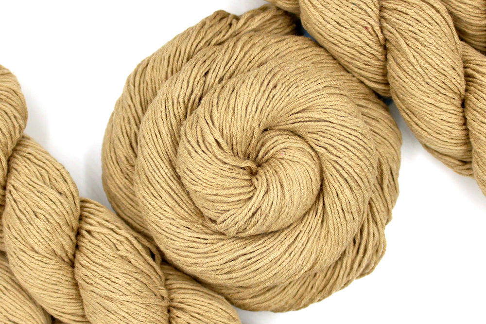 A skein of Vegan, golden tan, 100% Cotton, Sport Weight Yarn recycled by hand from unwanted sweaters swirled attractively in the center of the frame. 