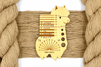 A skein of Vegan, golden tan, 100% Cotton, Sport Weight Yarn recycled by hand from unwanted sweaters draped over the center of the frame with one strand on top of a Llama shaped Yarn weight tool, to better illustrate the thickness of the yarn. 