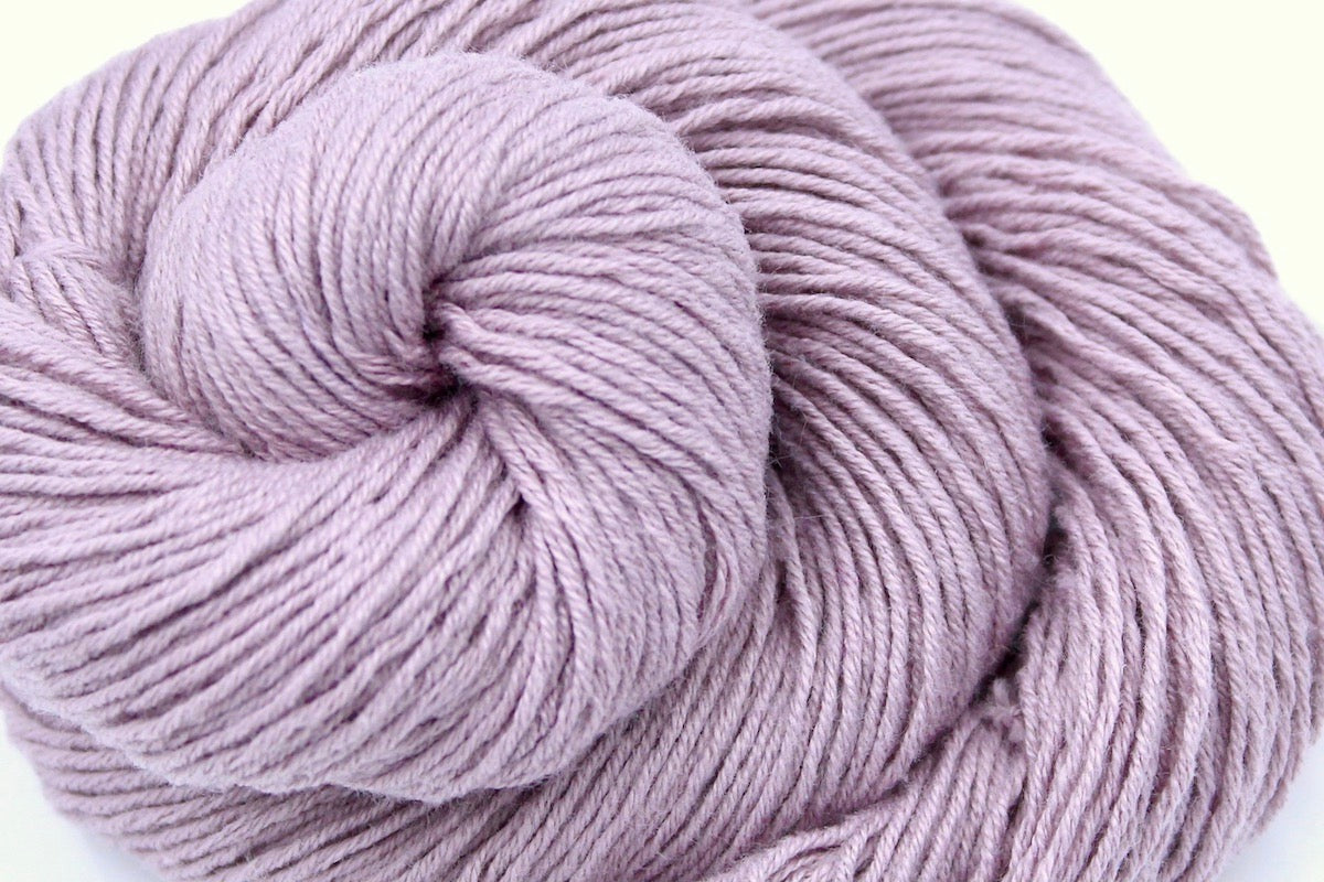 A close up shot of a skein of Vegan, Pastel Pinkish Purple, Cotton/ Acrylic, Fingering weight Yarn recycled by hand from unwanted sweaters beautifully coiled in the center of the frame. 