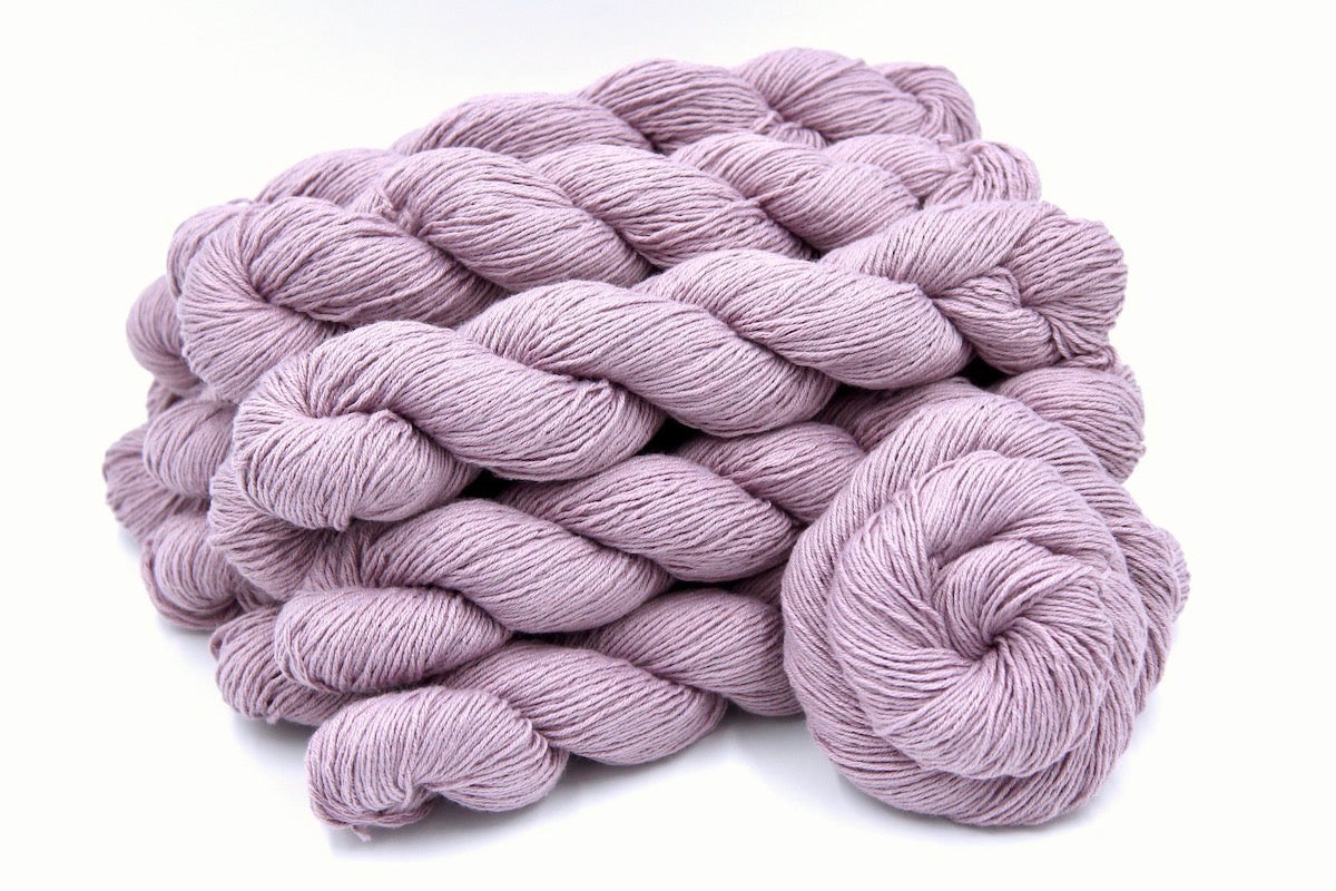 Several skeins of Vegan, Pastel Pinkish Purple, Cotton/ Acrylic, Fingering weight recycled by hand from unwanted sweaters stacked on top of each other attractively. 