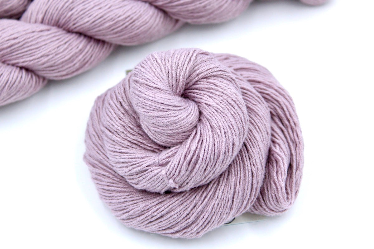 A skein of Vegan, Pastel Pinkish Purple, Cotton/ Acrylic, Fingering weight Yarn recycled by hand from unwanted sweaters swirled attractively in the center of the frame. 