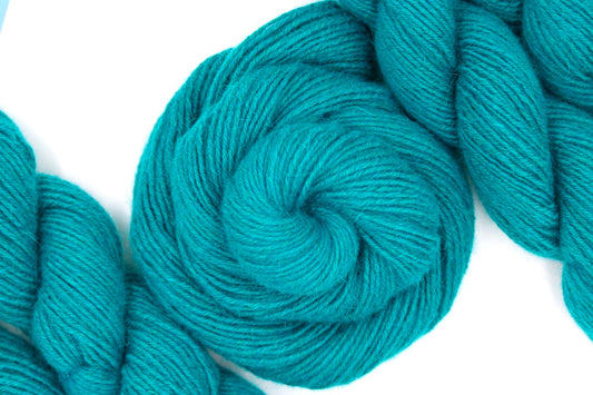 A skein of Deep Teal, Lamb’s Wool/ Angora/ Nylon, Dk weight Yarn recycled by hand from unwanted sweaters swirled attractively in the center of the frame. 