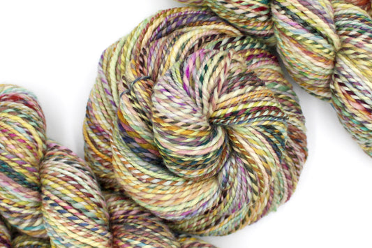 A one of a kind, Worsted Weight, hand dyed variegated skein of multicolored Green, Maroon, Pink, Yellow and Chartreuse, self-striping superwash wool Yarn coiled attractively in the center of the frame. 