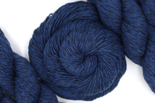 A skein of Vegan, Navy Blue/ Black, Cotton/ Acrylic, Fingering weight Yarn recycled by hand from unwanted sweaters swirled attractively in the center of the frame. 