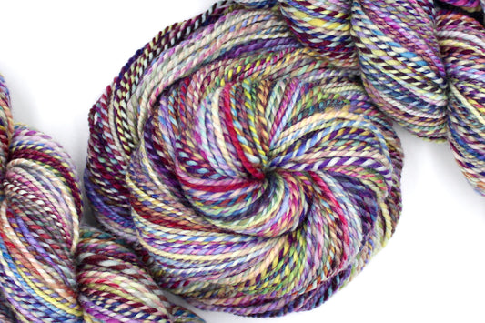 A one of a kind, Sport Weight, hand dyed variegated skein of multicolored Rainbow self-striping 100% Superwash Merino wool Yarn coiled attractively in the center of the frame. 