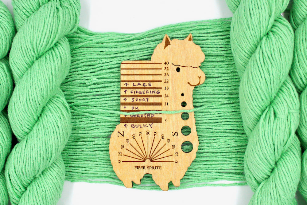 A skein of Vegan, vibrant light green, 100% Cotton, Worsted Weight Yarn recycled by hand from unwanted sweaters draped over the center of the frame with one strand on top of a Llama shaped Yarn weight tool, to better illustrate the thickness of the yarn. 