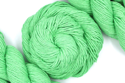A skein of Vegan, vibrant light green, 100% Cotton, Worsted Weight Yarn recycled by hand from unwanted sweaters swirled attractively in the center of the frame. 