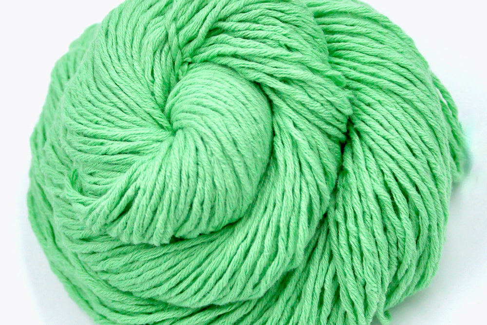 A close up shot of a skein of Vegan, vibrant light green, 100% Cotton, Worsted Weight Yarn recycled by hand from unwanted sweaters beautifully coiled in the center of the frame. 