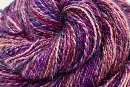 A close up view of a one of a kind, variegated skein of multicolored Peach, Pink, Purple, and Magenta self-striping wool Yarn. 