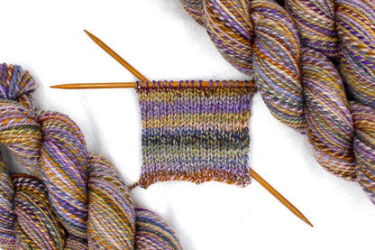 A sample swatch knitted on size 5 knitting needles from a one of a kind, Dk Weight, hand dyed Variegated skein of self striping Maroon, Pink, Cornflower Blue, and Lime Gr multicolored Purple, Lavender, Periwinkle, Taupe, Gold, and Orange self-striping Yarn, made of 100% Hand Dyed Merino Wool. 