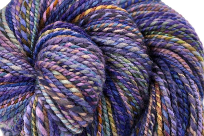 A close up view of a one of a kind, variegated skein of multicolored Purple, Blue, Green, Pink and Gold self-striping wool Yarn. 