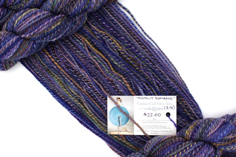 A one of a kind, hand dyed variegated skein of multicolored Purple, Blue, Green, Pink and Gold self-striping wool Yarn draped diagonally across the frame, so you can really see the color play. 