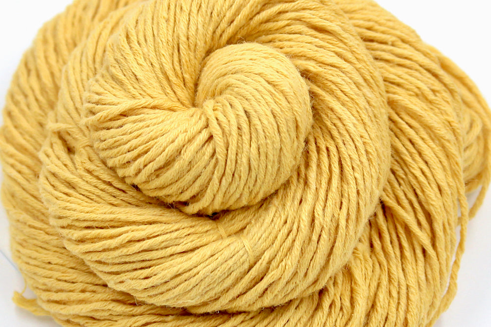 A close up shot of a skein of Vegan, Mustard Yellow, Cotten blend, DK Weight Yarn recycled by hand from unwanted sweaters beautifully coiled in the center of the frame. 