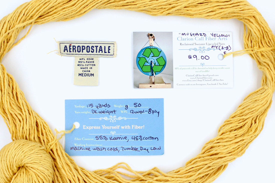 A skein of Vegan, Mustard Yellow, Cotten blend, DK Weight yarn encircling the sweater labels it was recycled from, as well as the hand written yarn tags detailing the specs of this recycled yarn to help you make your next project! 