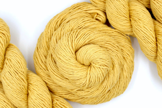 A skein of Vegan, Mustard Yellow, Cotten blend, DK Weight Yarn recycled by hand from unwanted sweaters swirled attractively in the center of the frame. 