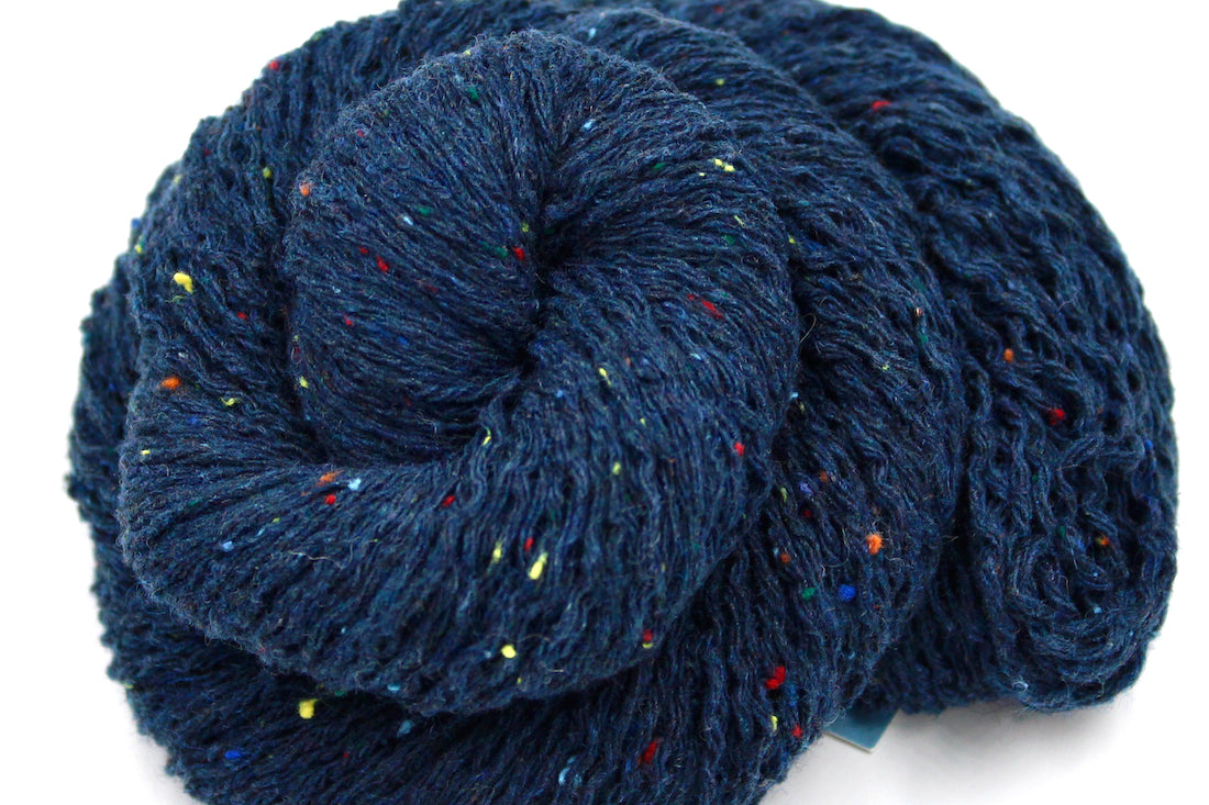 A close up shot of a skein of Dark Blue and Rainbow Tweed, Wool and Acrylic, Sport Weight Yarn recycled by hand from unwanted sweaters beautifully coiled in the center of the frame. 