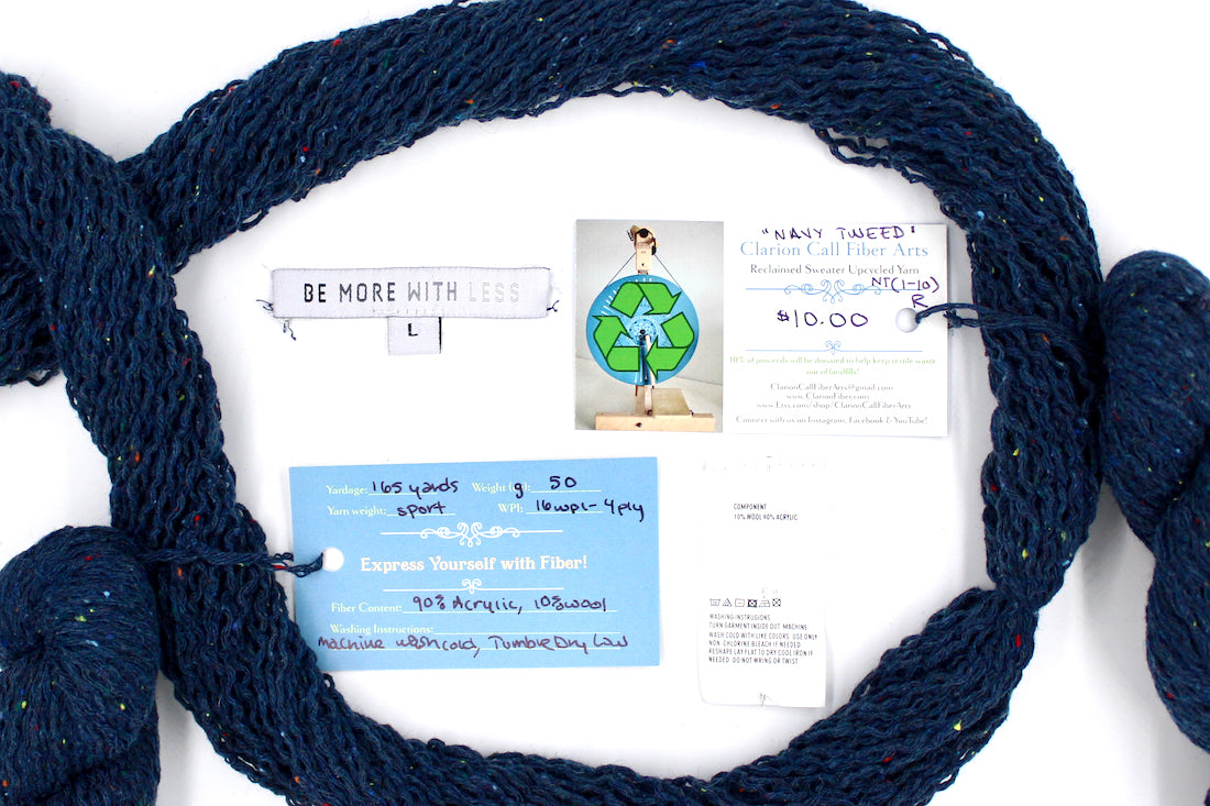 A skein of Dark Blue and Rainbow Tweed, Wool and Acrylic, Sport Weight yarn encircling the sweater labels it was recycled from, as well as the hand written yarn tags detailing the specs of this recycled yarn to help you make your next project! 