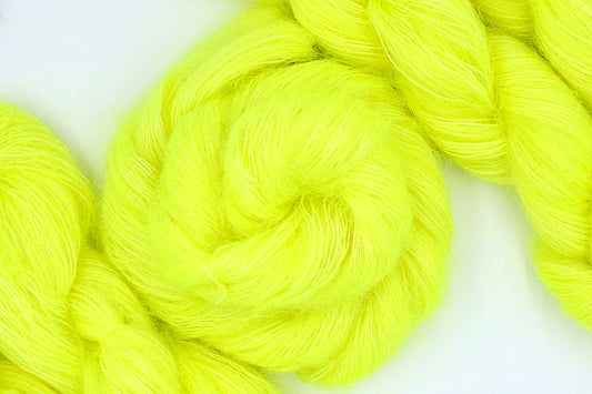 A skein of Neon Yellow, Kid Mohair/ Silk, Lace weight Yarn recycled by hand from unwanted sweaters swirled attractively in the center of the frame. 