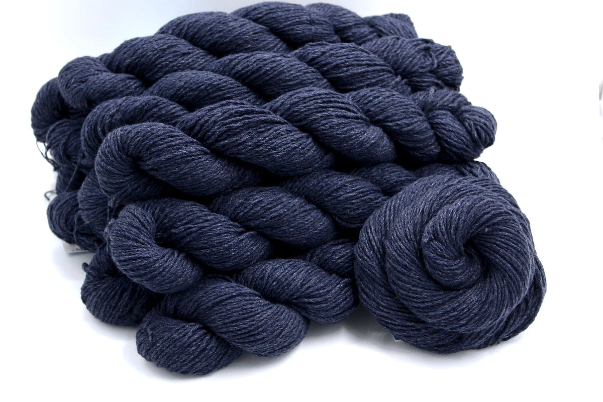 Several skeins of Vegan, Slate Navy Blue, Cotton/ Acrylic, Dk weight recycled by hand from unwanted sweaters stacked on top of each other attractively. 