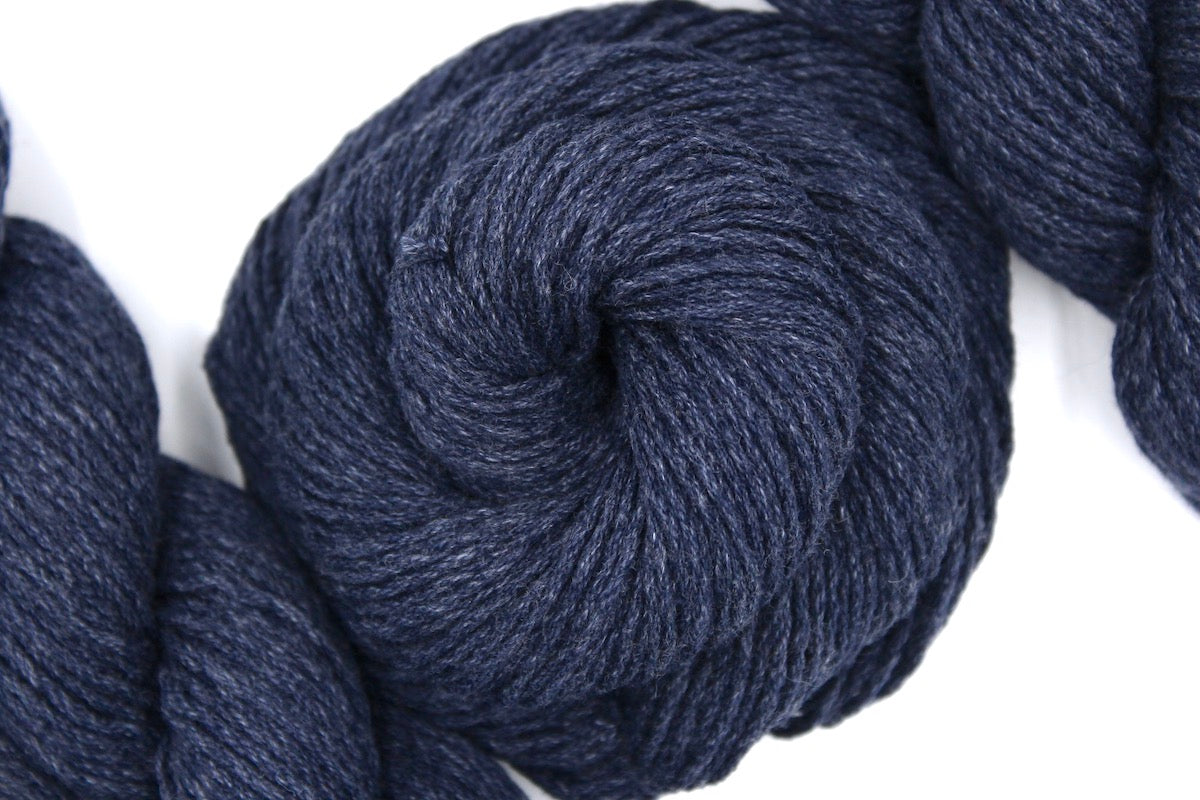 A skein of Vegan, Slate Navy Blue, Cotton/ Acrylic, Dk weight Yarn recycled by hand from unwanted sweaters swirled attractively in the center of the frame. 