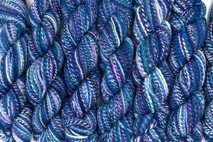 Six one of a kind, Dk Weight, hand dyed variegated skeins of multicolored Blue, and Purple self-striping Hand spun Yarn, made of 100% Hand Dyed Merino Wool lined up side by side. 