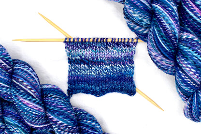 A sample swatch knitted on size 5 knitting needles from a one of a kind, Dk Weight, hand dyed variegated skein of multicolored Blue, and Purple self-striping Hand spun Yarn, made of 100% Hand Dyed Merino Wool. 