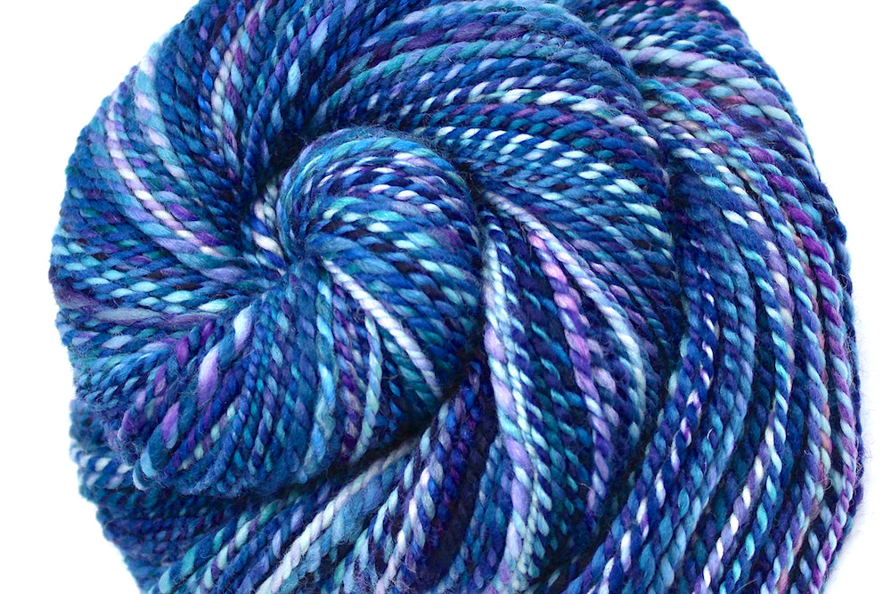 A close up view of a one of a kind, Dk Weight, hand dyed variegated skein of multicolored Blue, and Purple self-striping Hand spun Yarn, made of 100% Hand Dyed Merino Wool. 
