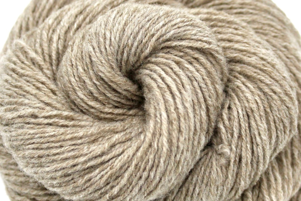 A close up shot of a skein of Tan/ Ecru/ Beige/ Taupe, Lamb's Wool/ Nylon, Sport weight Yarn recycled by hand from unwanted sweaters beautifully coiled in the center of the frame. 