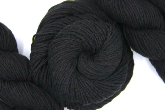 A skein of Vegan, Black, Cotton/ Acrylic, Worted weight Yarn recycled by hand from unwanted sweaters swirled attractively in the center of the frame. 