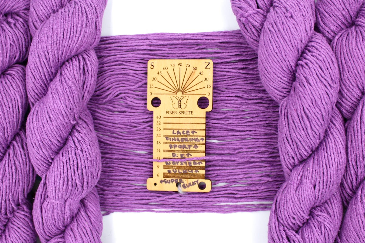 A skein of Vegan, Purplish Pink Orchid, 100% Cotton, Worsted Weight Yarn recycled by hand from unwanted sweaters draped over a Llama shaped Yarn weight tool. 