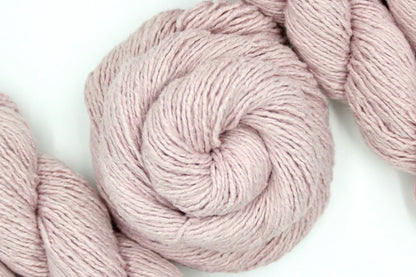 A skein of Vegan, Light Pastel Pink, Cotton/ Acrylic/ Polyester, Dk weight Yarn recycled by hand from unwanted sweaters swirled attractively in the center of the frame. 