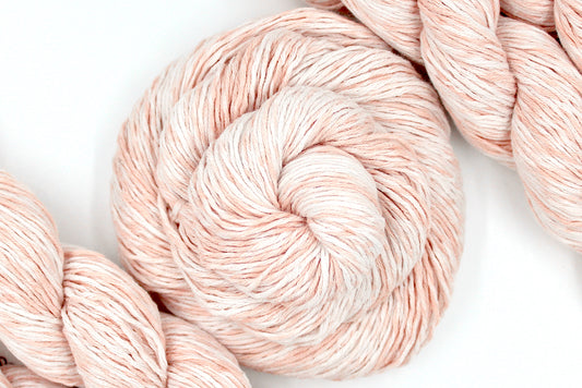A skein of Vegan, Variegated Pink and Cream, 100% Cotton, Sport Weight Yarn recycled by hand from unwanted sweaters swirled attractively in the center of the frame. 