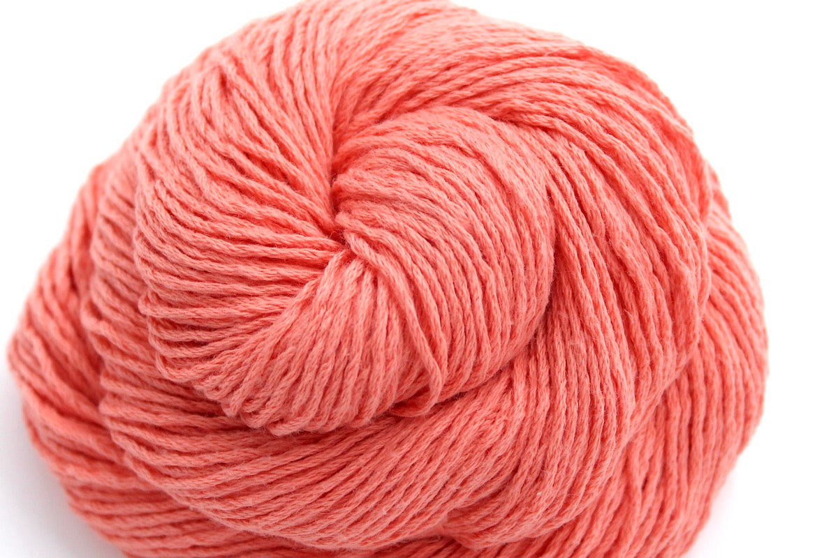 A close up shot of a skein of Vegan, Neon Peach, 100% Cotton, Sport weight Yarn recycled by hand from unwanted sweaters beautifully coiled in the center of the frame. 