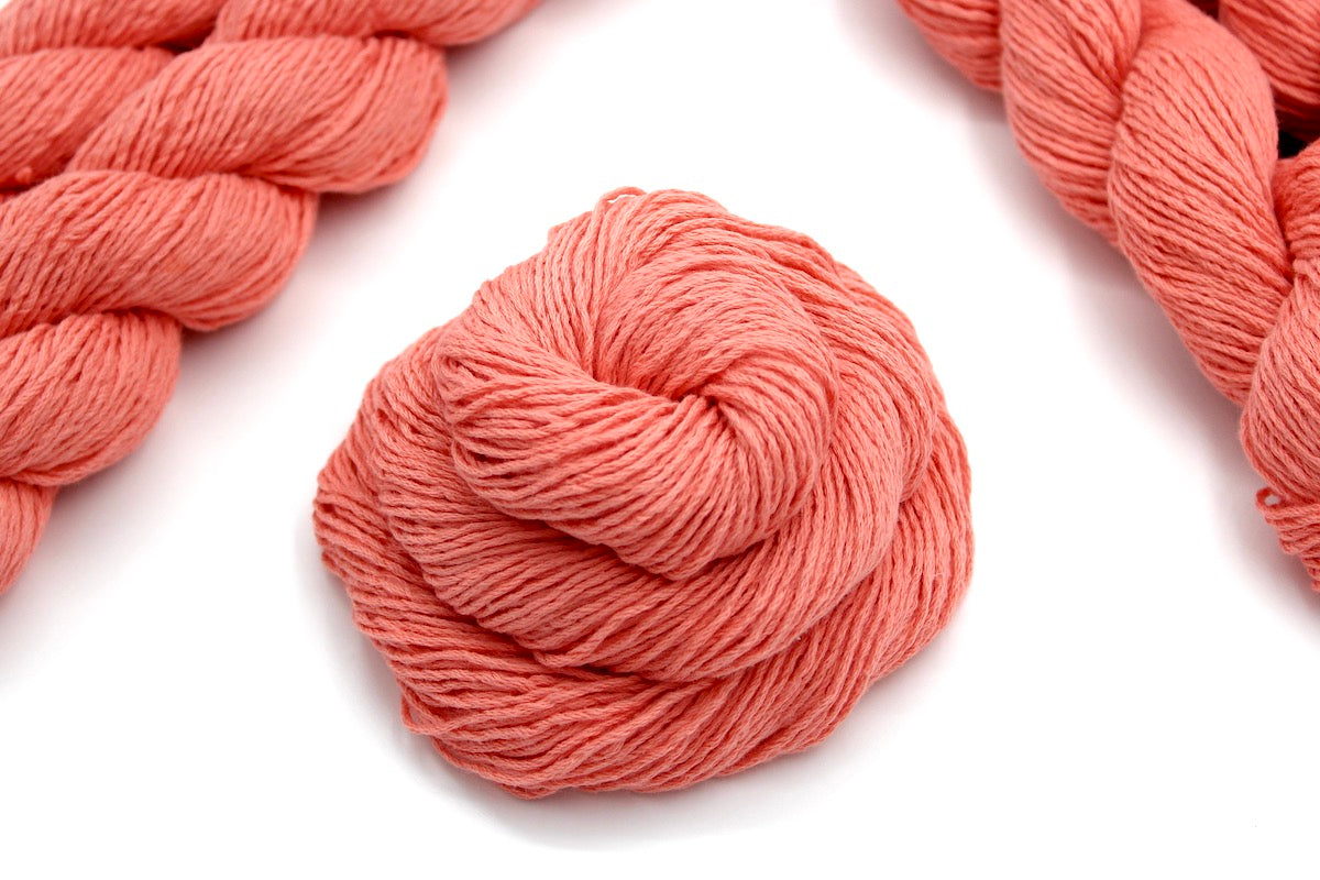 A skein of Vegan, Neon Peach, 100% Cotton, Sport weight Yarn recycled by hand from unwanted sweaters swirled attractively in the center of the frame. 