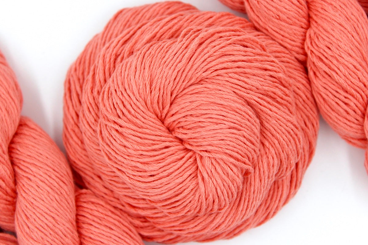 A skein of Vegan, Neon Peach, 100% Cotton, Sport weight Yarn recycled by hand from unwanted sweaters swirled attractively in the center of the frame. 