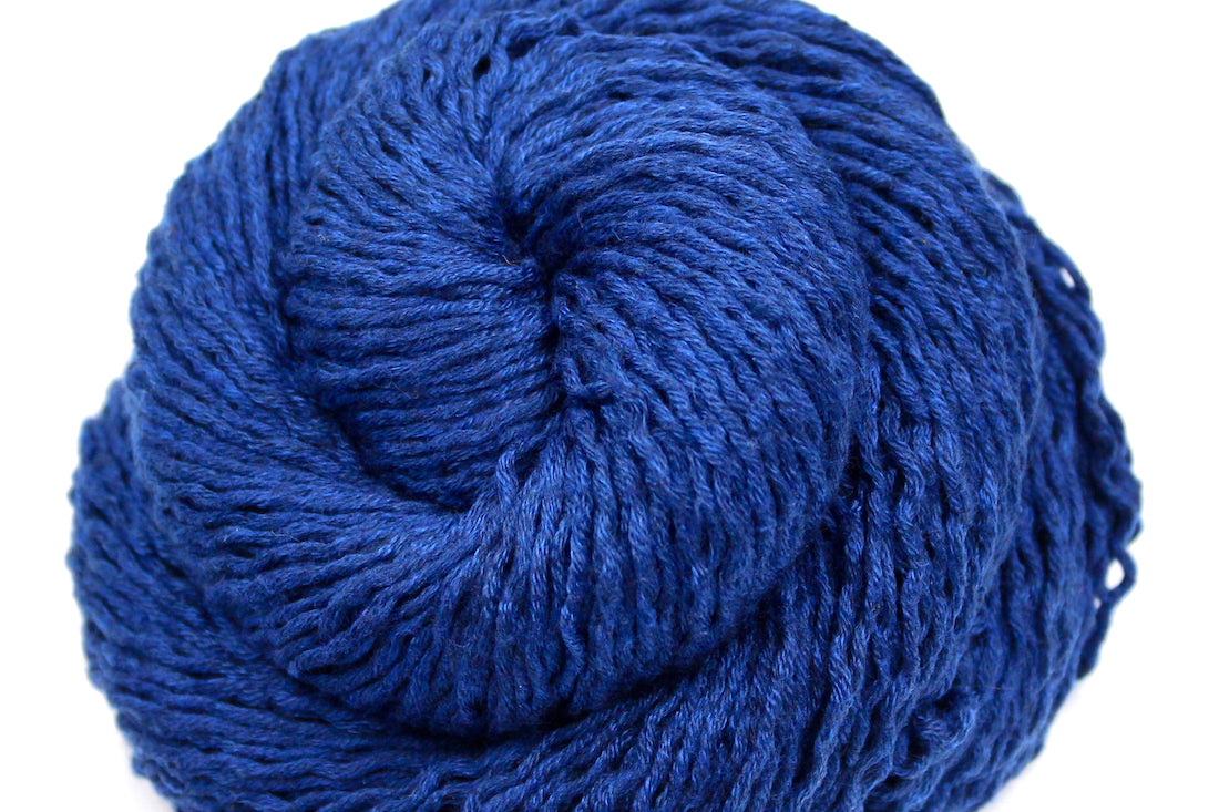 A close up shot of a skein of Vegan, Purplish Blue, 85% Polyester, 15% Nylon, Sport Weight Yarn recycled by hand from unwanted sweaters beautifully coiled in the center of the frame. 