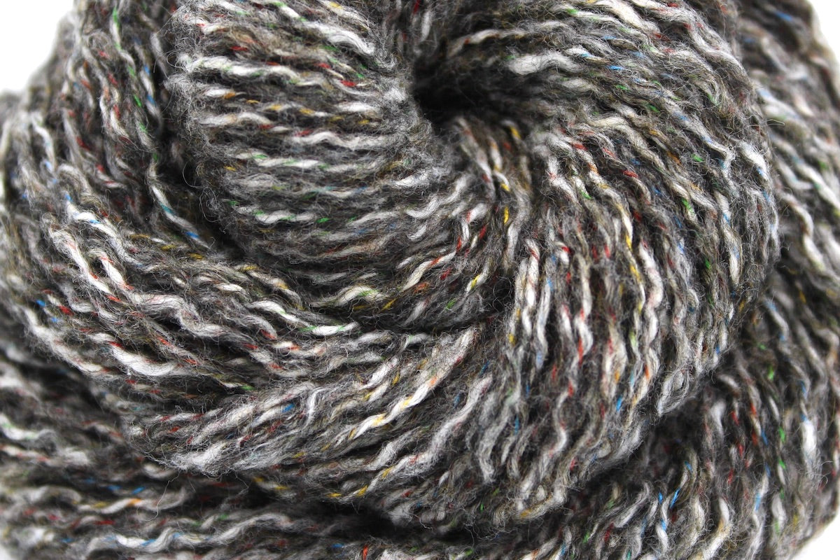 A close up shot of a skein of Vegan, Greyish Brown Variegated, Cotton/ Acrylic/ Polyester, DK weight Yarn recycled by hand from unwanted sweaters beautifully coiled in the center of the frame. 
