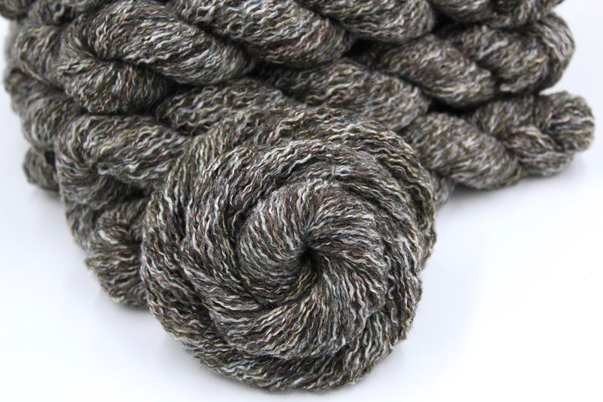 Several skeins of Vegan, Greyish Brown Variegated, Cotton/ Acrylic/ Polyester, DK weight recycled by hand from unwanted sweaters stacked on top of each other attractively. 