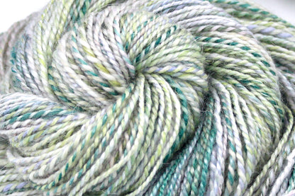 A close up view of a one of a kind, variegated skein of multicolored pastel Green, Lavender, and Pink self-striping wool Yarn. 